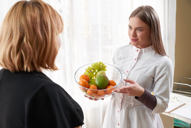 Ritratto di giovane nutrizionista femminile sorridente nella sala di consultazione. Fare un programma di dieta. Giovane donna visitando il nutrizionista nella clinica di perdita di peso