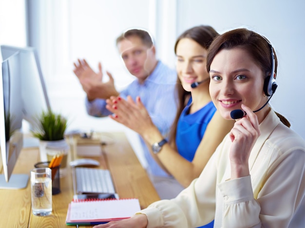 Ritratto di giovane operatore di call center che indossa la cuffia con i colleghi che lavorano in background in ufficio