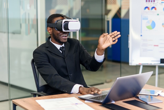 Ritratto di giovane professionista afroamericano che utilizza realtà virtuale aumentata nell'ufficio moderno del sottotetto. Tecnologia VR