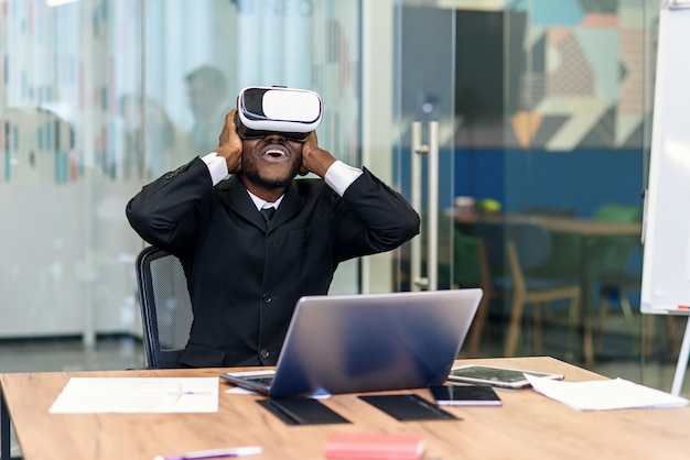 Ritratto di giovane professionista afroamericano che utilizza realtà virtuale aumentata nell'ufficio moderno del sottotetto. Tecnologia VR