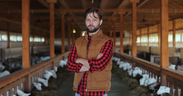 Ritratto di giovane proprietario di agricoltore che guarda la fotocamera sullo sfondo della fattoria di capre Concetto di produzione di allevamento biologico Moderna azienda di allevamento di bestiame