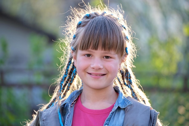 Ritratto di giovane ragazza adolescente sorridente felice in abiti casual con nastri blu in lunghe trecce all'aperto in estate o in primavera