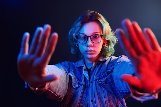 Ritratto di giovane ragazza alternativa con gli occhiali con i capelli verdi in luce al neon rossa e blu in studio