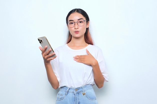 Ritratto di giovane ragazza asiatica stupita in maglietta bianca che tiene il telefono cellulare isolato su sfondo bianco