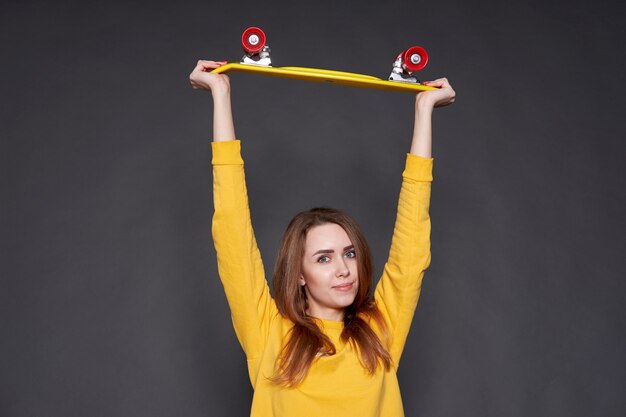 Ritratto di giovane ragazza attraente positiva che porta camicetta e blue jeans gialle che tengono pattino giallo.