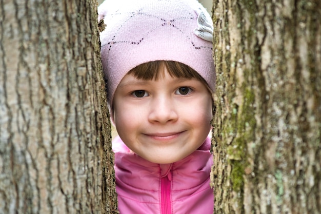 Ritratto di giovane ragazza carina bambino che indossa giacca rosa e cappuccio in piedi tra gli alberi