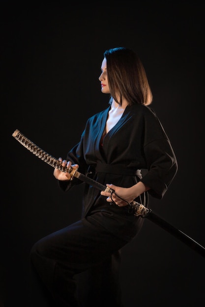 Ritratto di giovane ragazza castana di kung fu con wakizashi su sfondo nero