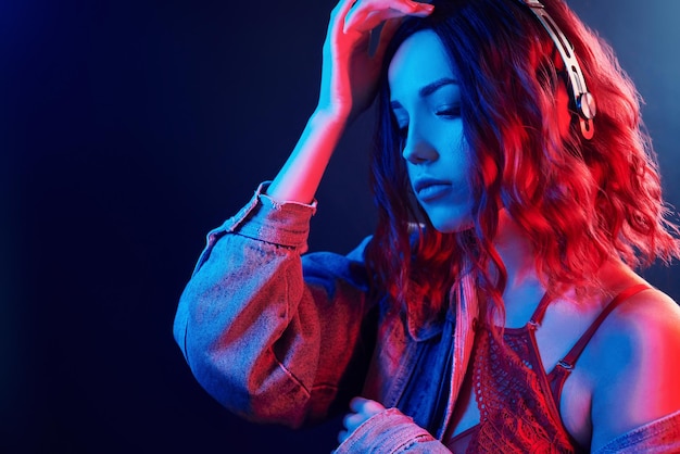 Ritratto di giovane ragazza che ascolta musica in cuffia al neon rosso e blu in studio