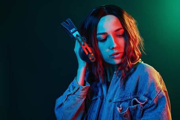 Ritratto di giovane ragazza che ascolta musica in cuffia al neon rosso e blu in studio