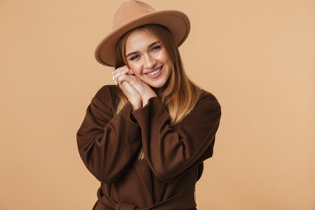 Ritratto di giovane ragazza che indossa cappello e cappotto sorridente isolato su beige