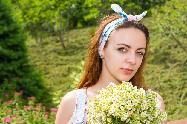 Ritratto di giovane ragazza che tiene in mano un grande mazzo di piccoli fiori bianchi mentre sta in piedi nel parco