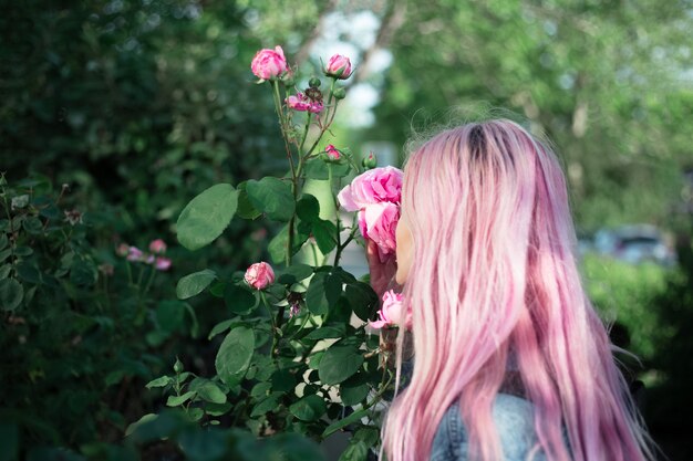 Ritratto di giovane ragazza con i capelli rosa sniffare fiore rosa.