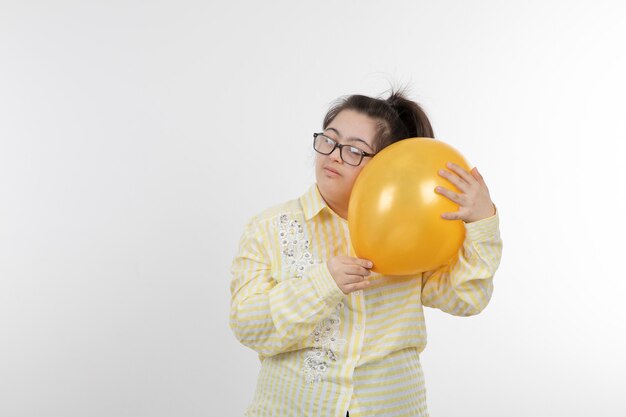 Ritratto di giovane ragazza con una sindrome di Down che indossa la maglietta a scacchi gialla tenendo il pallone ad aria