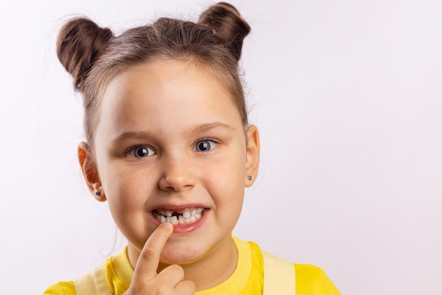 Ritratto di giovane ragazza faccia con la bocca aperta che punta al dente da latte anteriore mancante con il dito guardando la fotocamera su sfondo bianco Primi denti che cambiano andando dal dentista per fare il trattamento dei denti