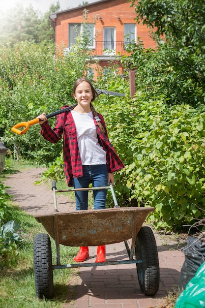 Ritratto di giovane ragazza felice in posa con carriola e pala in giardino al giorno di sole