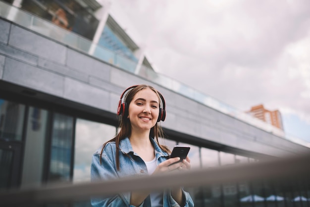 Ritratto di giovane ragazza hipster che gode di un volume elevato con gli auricolari tramite app sul cellulare moderno