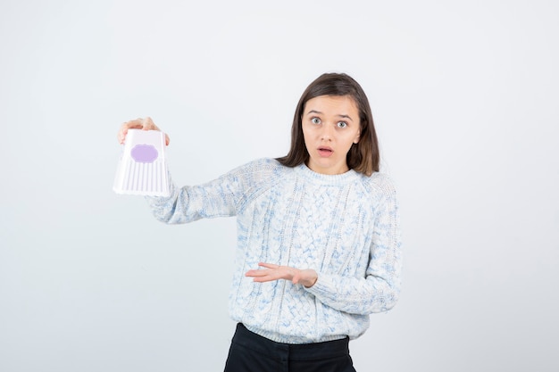 Ritratto di giovane ragazza in maglione lavorato a maglia che mostra scatola vuota di popcorn.