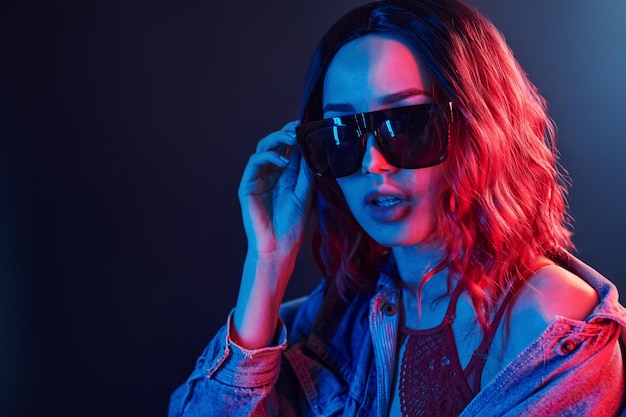 Ritratto di giovane ragazza in occhiali da sole in neon rosso e blu in studio