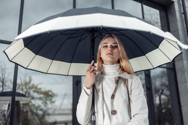 Ritratto di giovane ragazza in trench con ombrello vicino al centro business