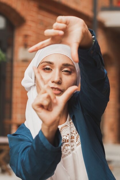 Ritratto di giovane ragazza musulmana che fa una cornice della fotocamera con le dita all'aperto