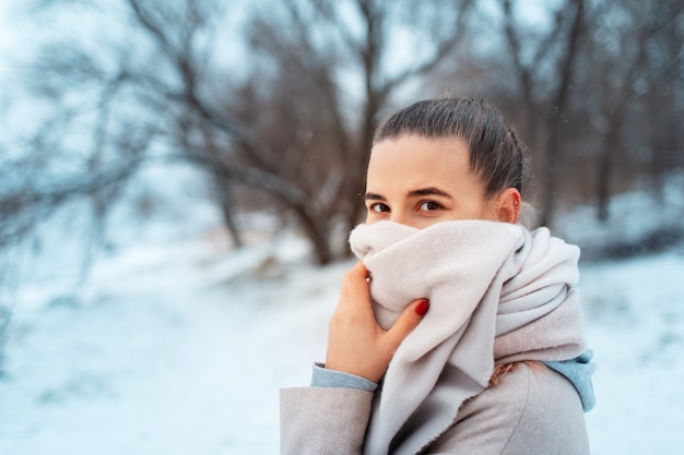 Ritratto di giovane ragazza nel parco in giornata invernale, indossa una sciarpa, sullo sfondo di alberi sfocati.