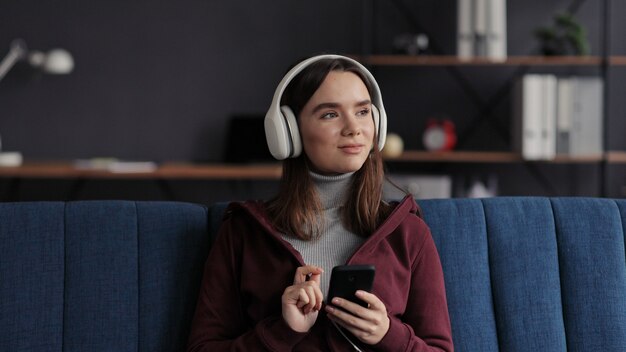Ritratto di giovane ragazza sorridente che indossa le cuffie, scegliendo i brani musicali preferiti nell'applicazione mobile
