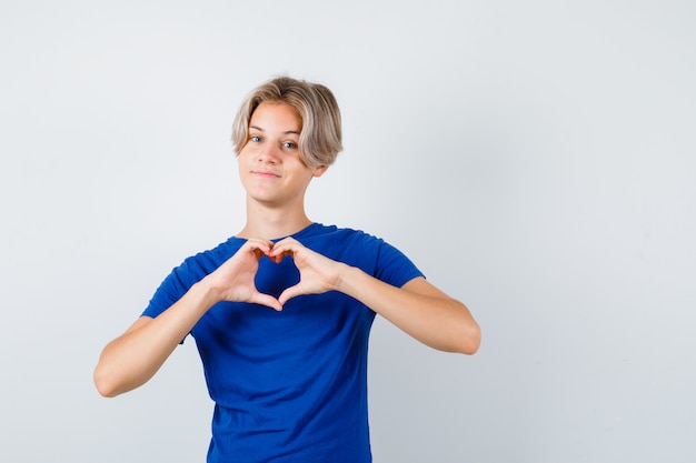 Ritratto di giovane ragazzo adolescente che mostra il gesto del cuore in maglietta blu e sembra una vista frontale allegra