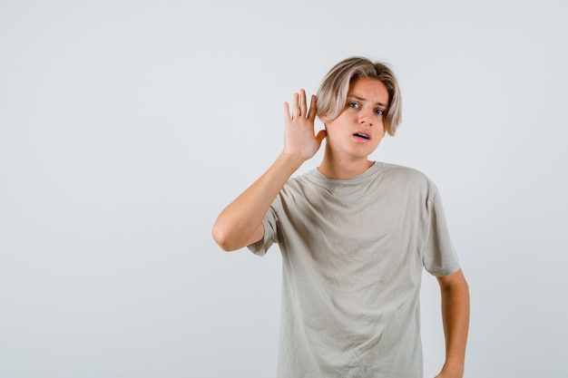 Ritratto di giovane ragazzo adolescente con la mano dietro l'orecchio in maglietta e guardando confuso vista frontale