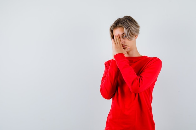 Ritratto di giovane ragazzo adolescente con le mani in gesto di preghiera in maglione rosso e guardando speranzoso vista frontale