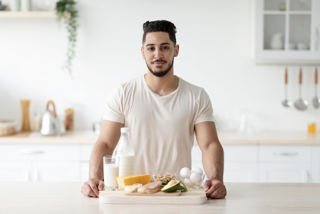 Ritratto di giovane ragazzo arabo attraente con prodotti proteici sani in posa in cucina