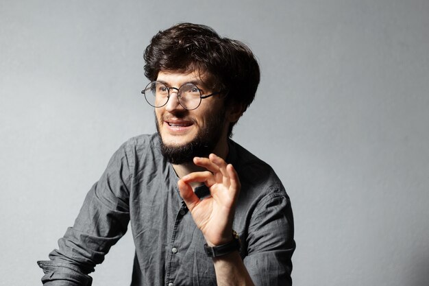 Ritratto di giovane ragazzo barbuto con i capelli arruffati e occhiali, guardando lontano e parlando