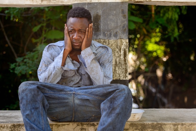 Ritratto di giovane senzatetto uomo africano sul ponte nelle strade all'aperto