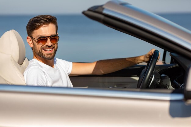 Ritratto di giovane sorridente seduto in cabriolet e guardando la telecamera