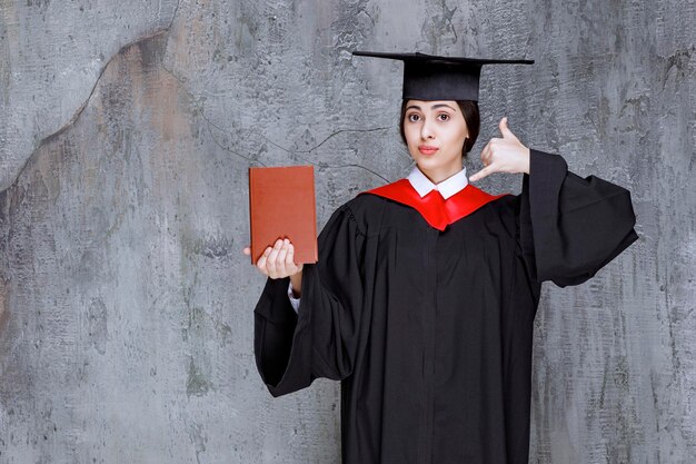 Ritratto di giovane studente laureato con libro in piedi contro il muro. Foto di alta qualità