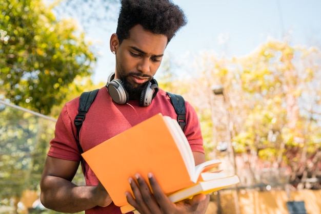 Ritratto di giovane studente universitario afro leggendo e studiando con il suo libro nel campus. Concetto di educazione e stile di vita.