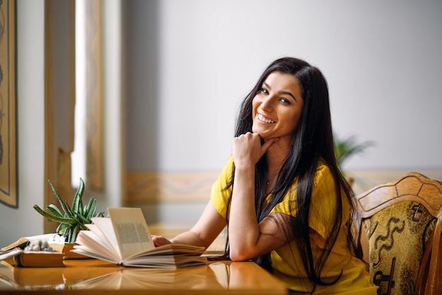 Ritratto di giovane studentessa entusiasta sorridente che studia con un libro alla biblioteca