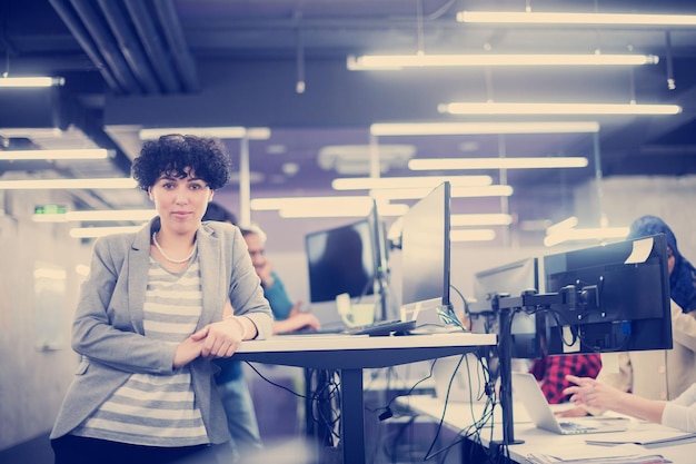 Ritratto di giovane sviluppatore di software femminile in un ufficio di avvio occupato con il suo team aziendale multietnico in background