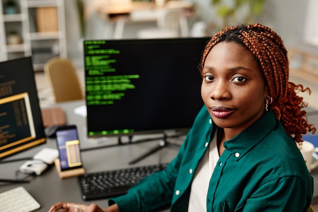 Ritratto di giovane sviluppatore femminile che guarda l'obbiettivo contro il codice di programmazione sullo schermo del computer