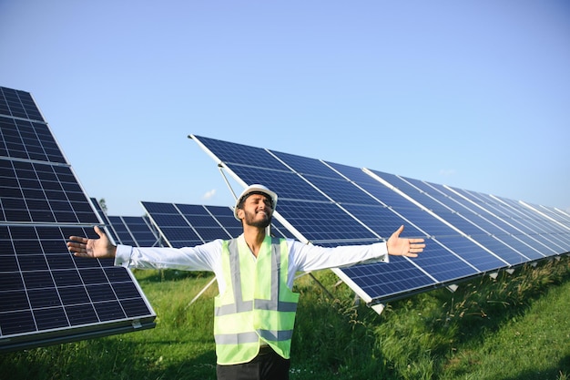 Ritratto di giovane tecnico indiano che indossa elmetto bianco in piedi vicino a pannelli solari contro il cielo blu Operaio industriale installazione sistema solare concetto di generazione di energia verde rinnovabile