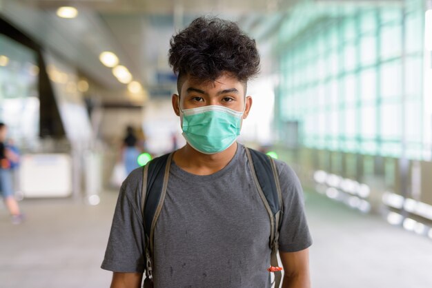 Ritratto di giovane turista asiatico come zaino in spalla con maschera per la protezione dall'epidemia di coronavirus alla stazione dello sky train