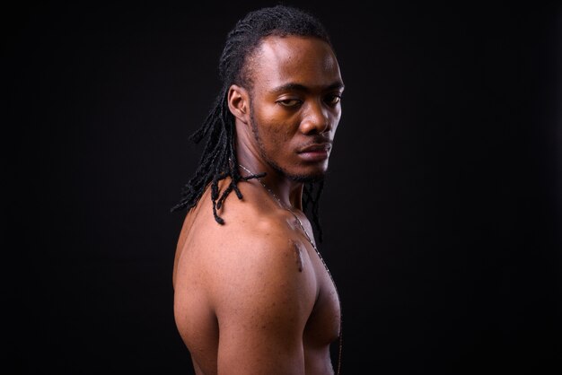 ritratto di giovane uomo africano bello con i dreadlocks a torso nudo sul nero