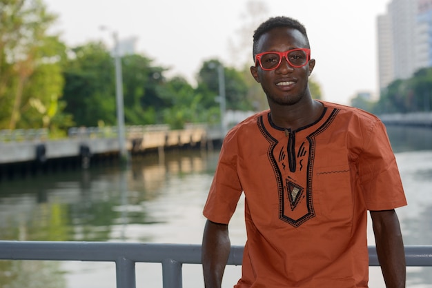 Ritratto di giovane uomo africano che indossa abiti tradizionali contro la vista del fiume in città all'aperto