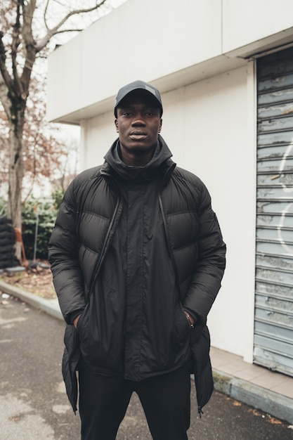 Ritratto di giovane uomo africano che sta nella via e che guarda macchina fotografica