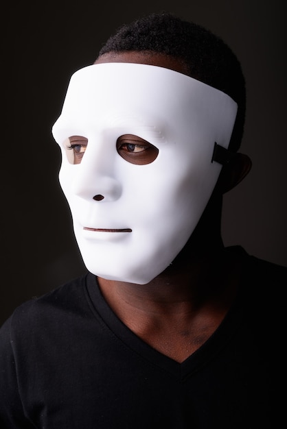 Ritratto di giovane uomo africano nero in camera oscura che indossa la maschera