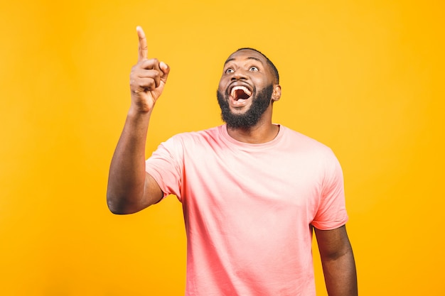 Ritratto di giovane uomo afroamericano bello felice con nel sorridere casuale, indicando da parte con il dito, guardando con l'espressione eccitata del viso