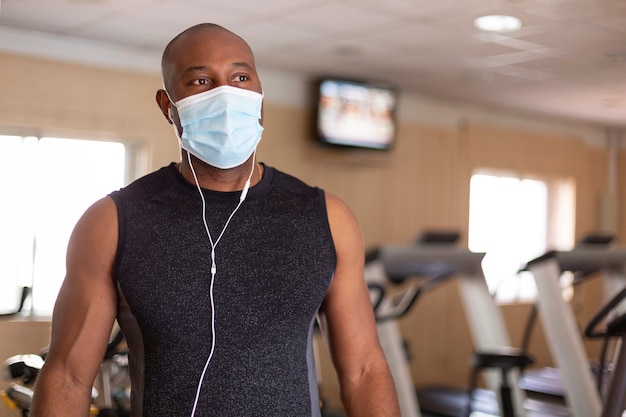 Ritratto di giovane uomo afroamericano in abiti sportivi. È in palestra e indossa una mascherina medica per precauzione per evitare il contagio.