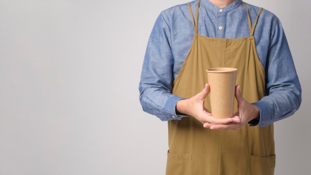 Ritratto di giovane uomo asiatico che indossa il grembiule tenendo la tazza di carta su bianco