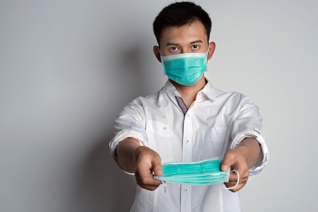 ritratto di giovane uomo asiatico che indossa maschera e offre maschera mentre guarda la telecamera