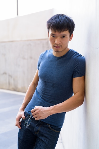 Ritratto di giovane uomo asiatico che si appoggia sulla parete all'aperto