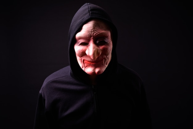 Ritratto di giovane uomo asiatico con felpa con cappuccio e maschera horror su fondo nero